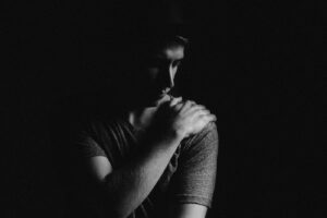 Man sitting alone in a dark room with arms crossed, appearing withdrawn