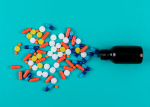 Colorful pills and capsules spilling from a bottle on a teal background