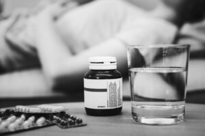 Black-and-white image of medication bottles and a glass of water on a table