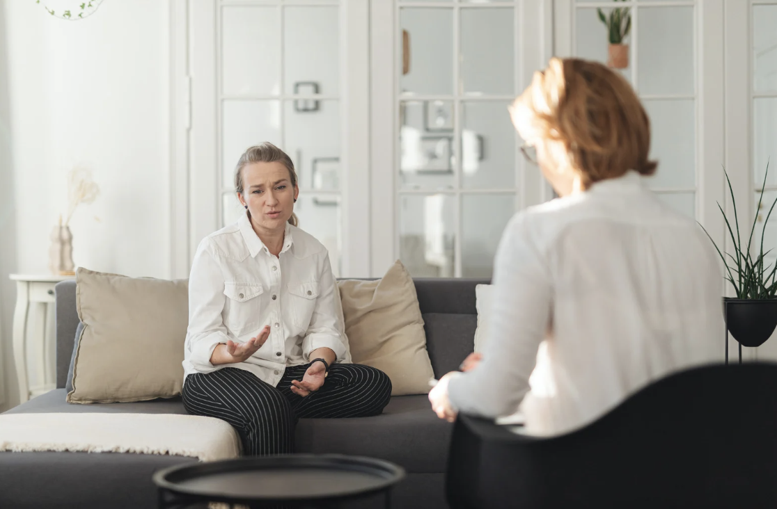 woman on couch looking concerned speaking to another woman therapist